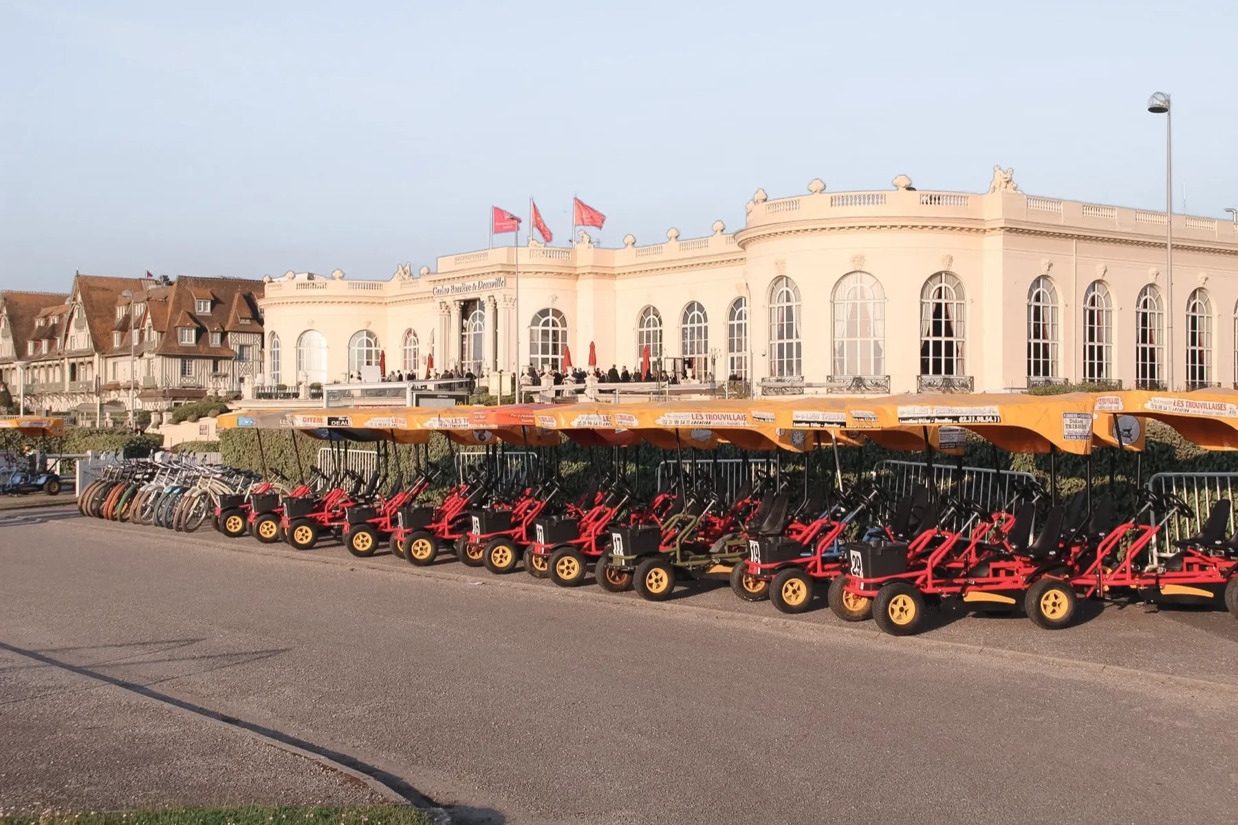 Une longue file de rosalies rouges à auvent jaune alignées le long de la promenade, devant la façade blanche du casino de Deauville et ses drapeaux.