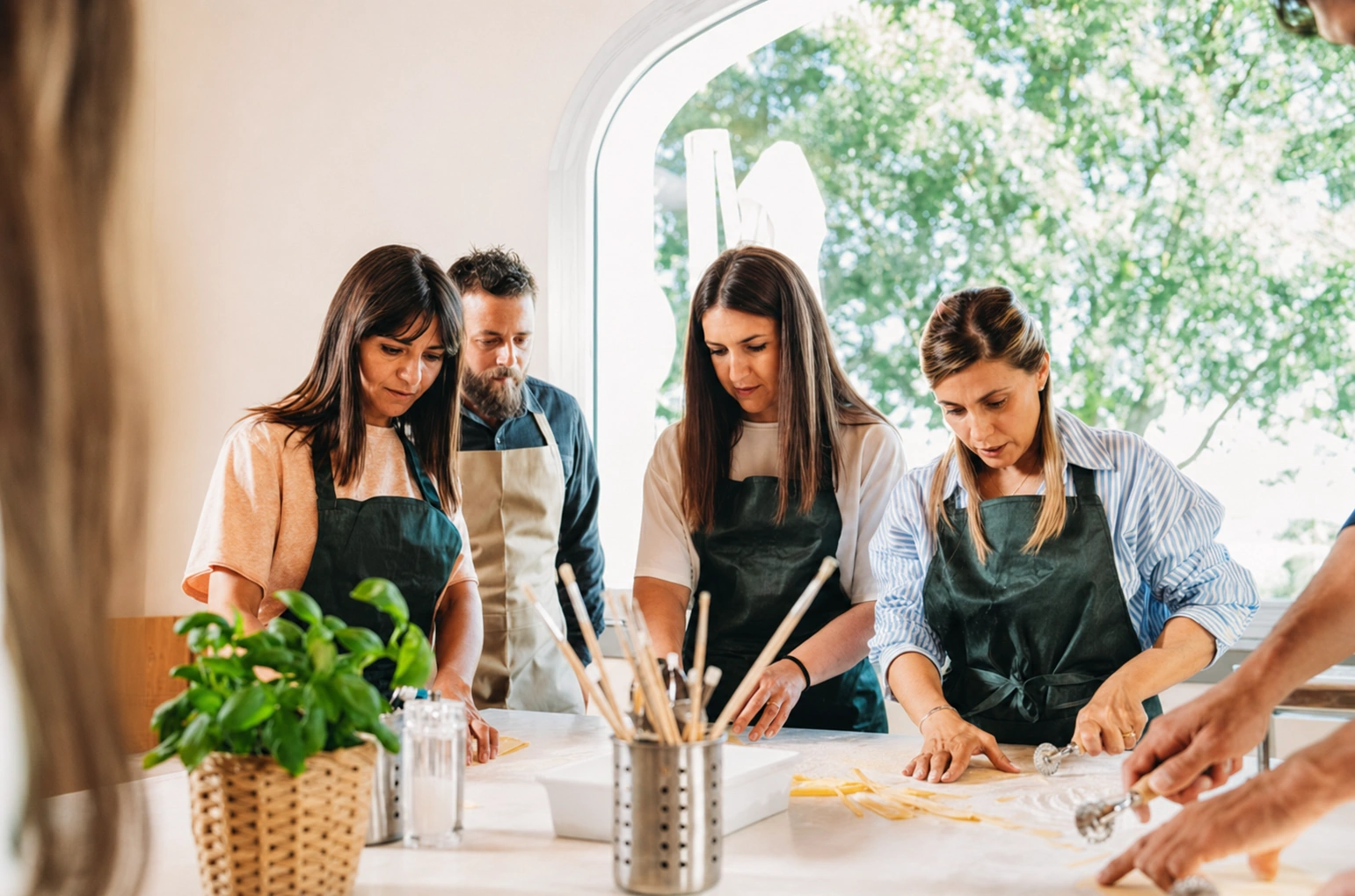 Quatre participants en tablier façonnent des pâtes fraîches autour d'un plan de travail, guidés par un chef.