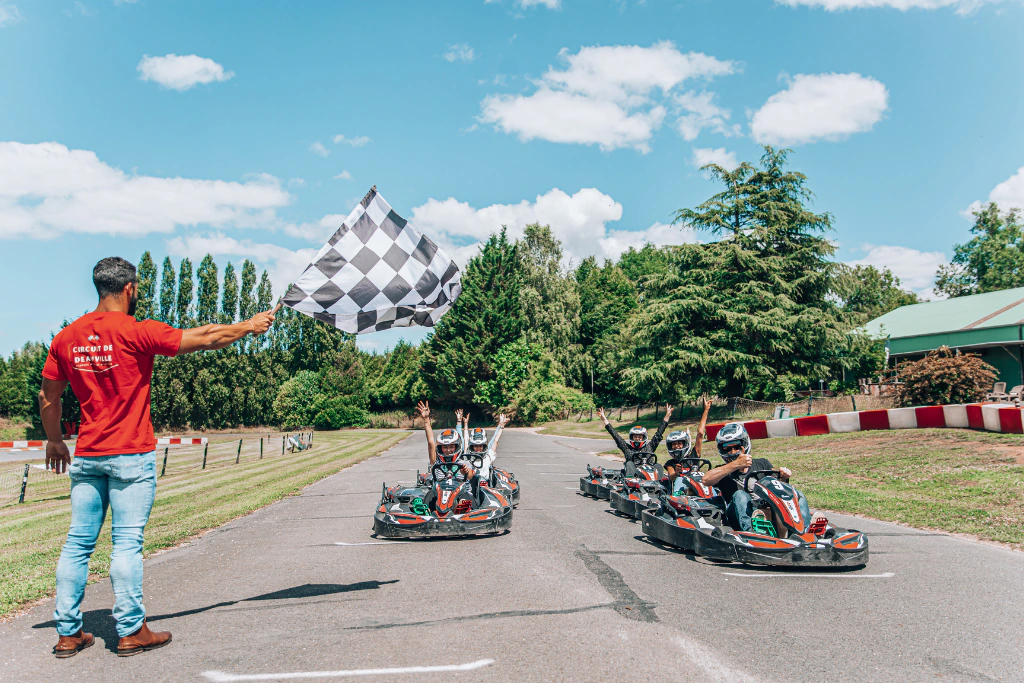 Deux karts franchissent la ligne d'arrivée bras levés, un commissaire agitant le drapeau à damier sur le circuit de Deauville.