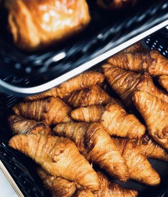 Des croissants et des viennoiseries dorés serrés dans des corbeilles noires.