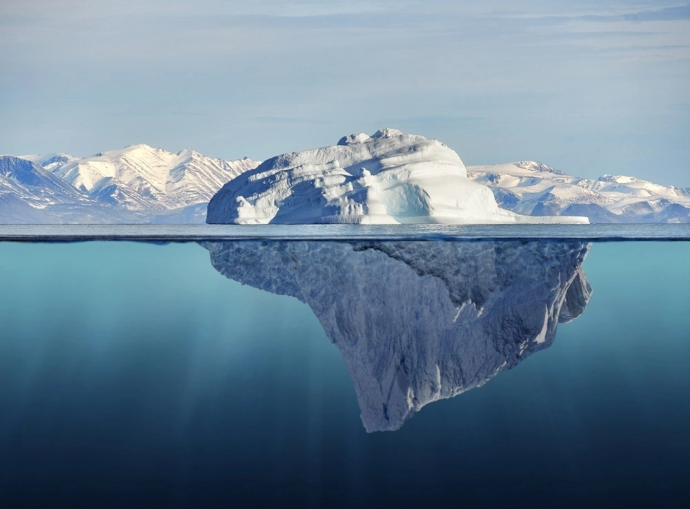 Un iceberg photographié de part et d'autre de la surface : la partie émergée est modeste, la masse immergée occupe presque toute l'image.