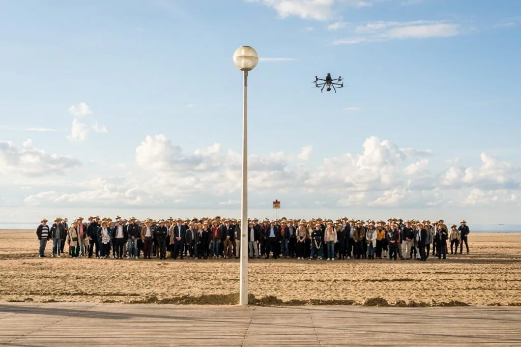 Photo de groupe d'un séminaire d'entreprise sur la plage de Deauville : plusieurs rangs de participants alignés au pied des Planches, survolés par un drone.