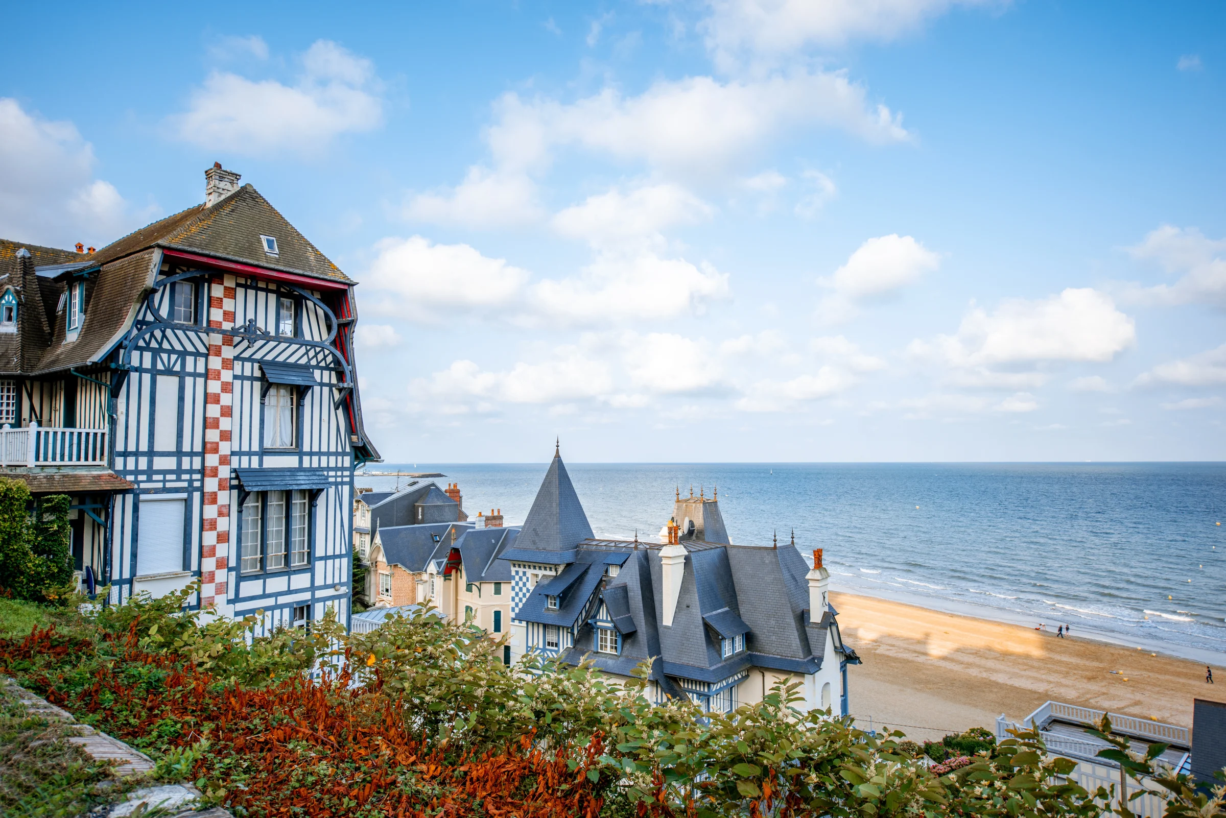 Vue plongeante sur les villas balnéaires normandes à colombages et toits d'ardoise qui dominent la plage, la mer et le sable s'étendant jusqu'à l'horizon.